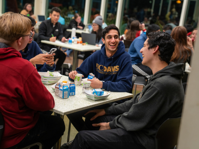 three students talking while seated in the busy Coffee House
