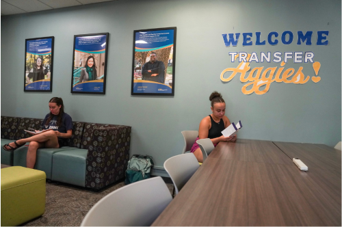 Two students sitting in the Transfer Center with "Welcome Transfer Aggies" sign in background
